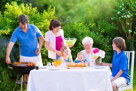 38675819 - grill barbecue backyard party. happy big family - young mother and father with kids, teen age son, cute toddler daughter and a little baby, enjoying bbq lunch with grandmother eating grilled meat in the garden with salad and bread.